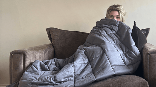 Person wrapped in a gray weighted blanket on a cozy couch, promoting comfort and relaxation.