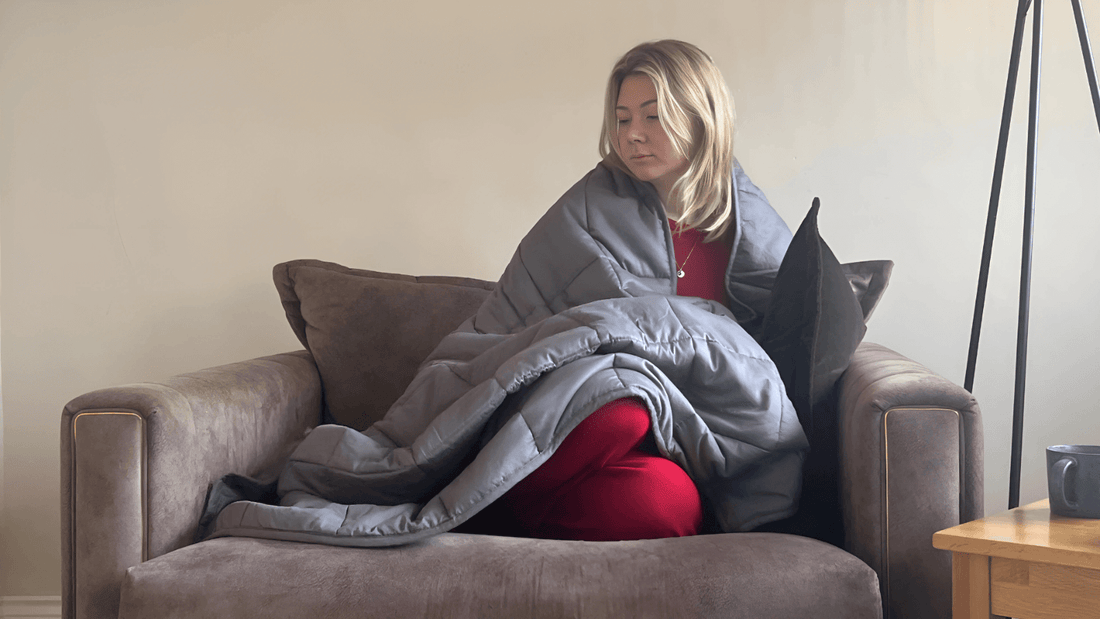 A young woman relaxing on a sofa, wrapped in a cozy gray weighted blanket for comfort and warmth.