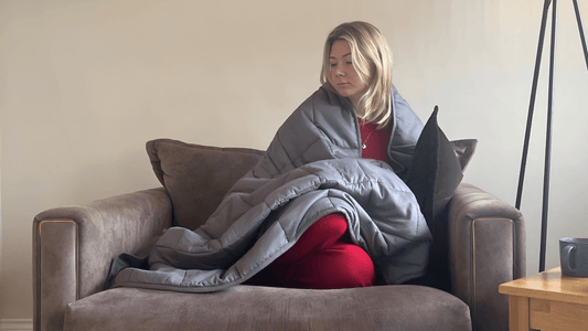Adult woman wrapped in a weighted blanket sitting on a couch, seeking calm and comfort.