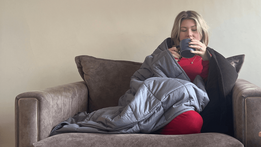 A young woman relaxing on a sofa, wrapped in a cozy gray weighted blanket for comfort and warmth.