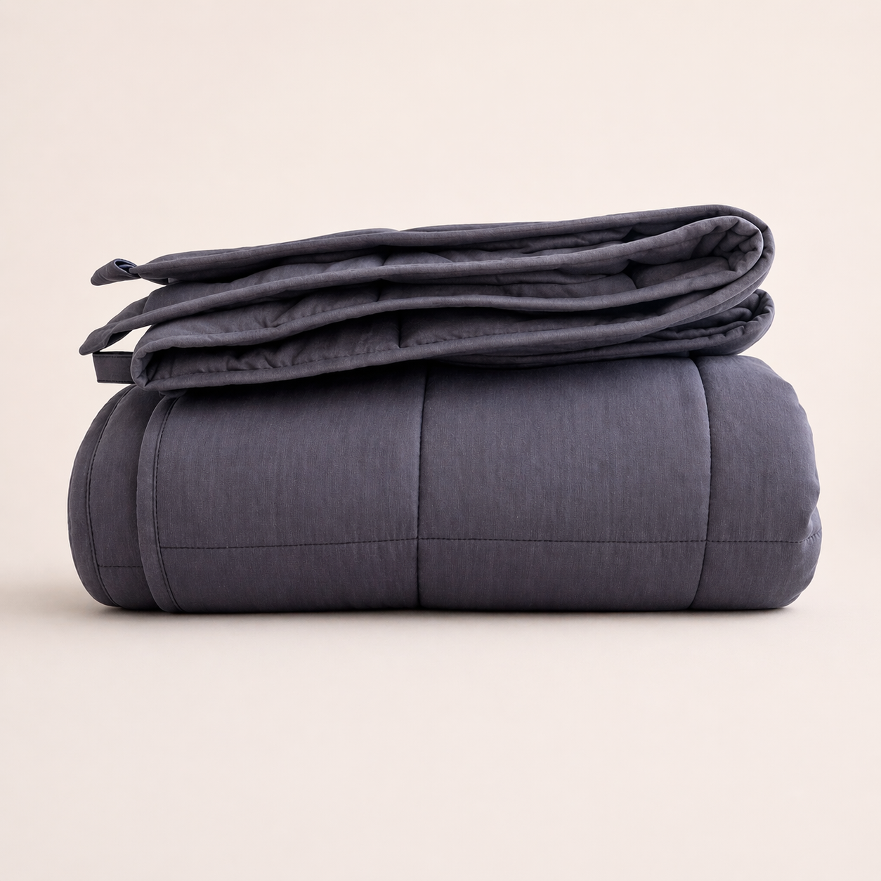 Folded dark gray weighted blanket on a beige background